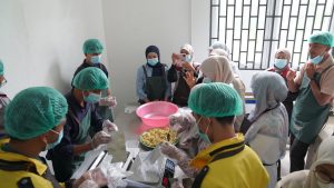 Participants wear aprons, hairnets, masks, and gloves as they portion and pack emergency food into pouches at TDMRC USK on 7 October 2026.